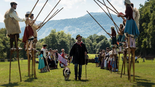 Des echassiers forment une allée pour un berger et son chien à la Fête des Bergers d'Aramits