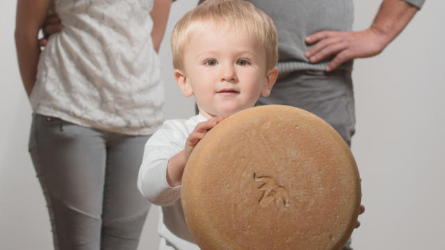 Un couple de producteurs de fromage de brebis, leur fils de tient une tomme de fromage de brebis au premier plan.