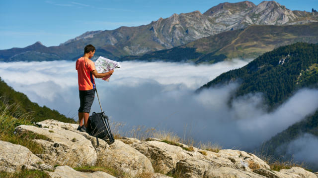 Randonneur regarde une carte devant une mer de nuages