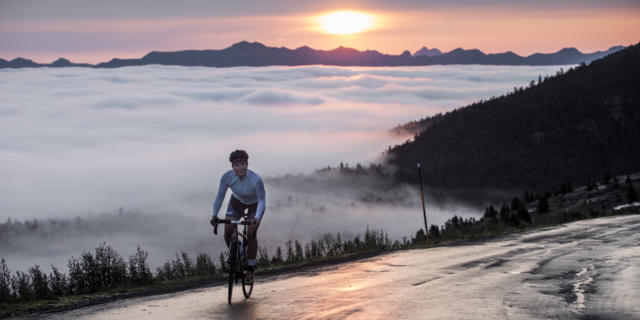 Une cycliste au sommet d'un col avec vue sur le coucher de soleil et les montagnes