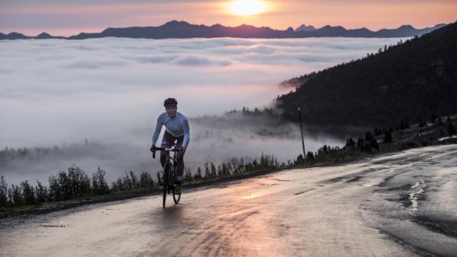 Une cycliste au sommet d'un col avec vue sur le coucher de soleil et les montagnes