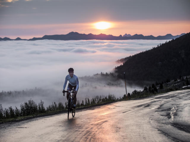 Une cycliste au sommet d'un col avec vue sur le coucher de soleil et les montagnes