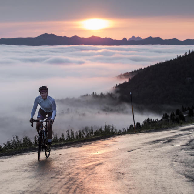 Une cycliste au sommet d'un col avec vue sur le coucher de soleil et les montagnes